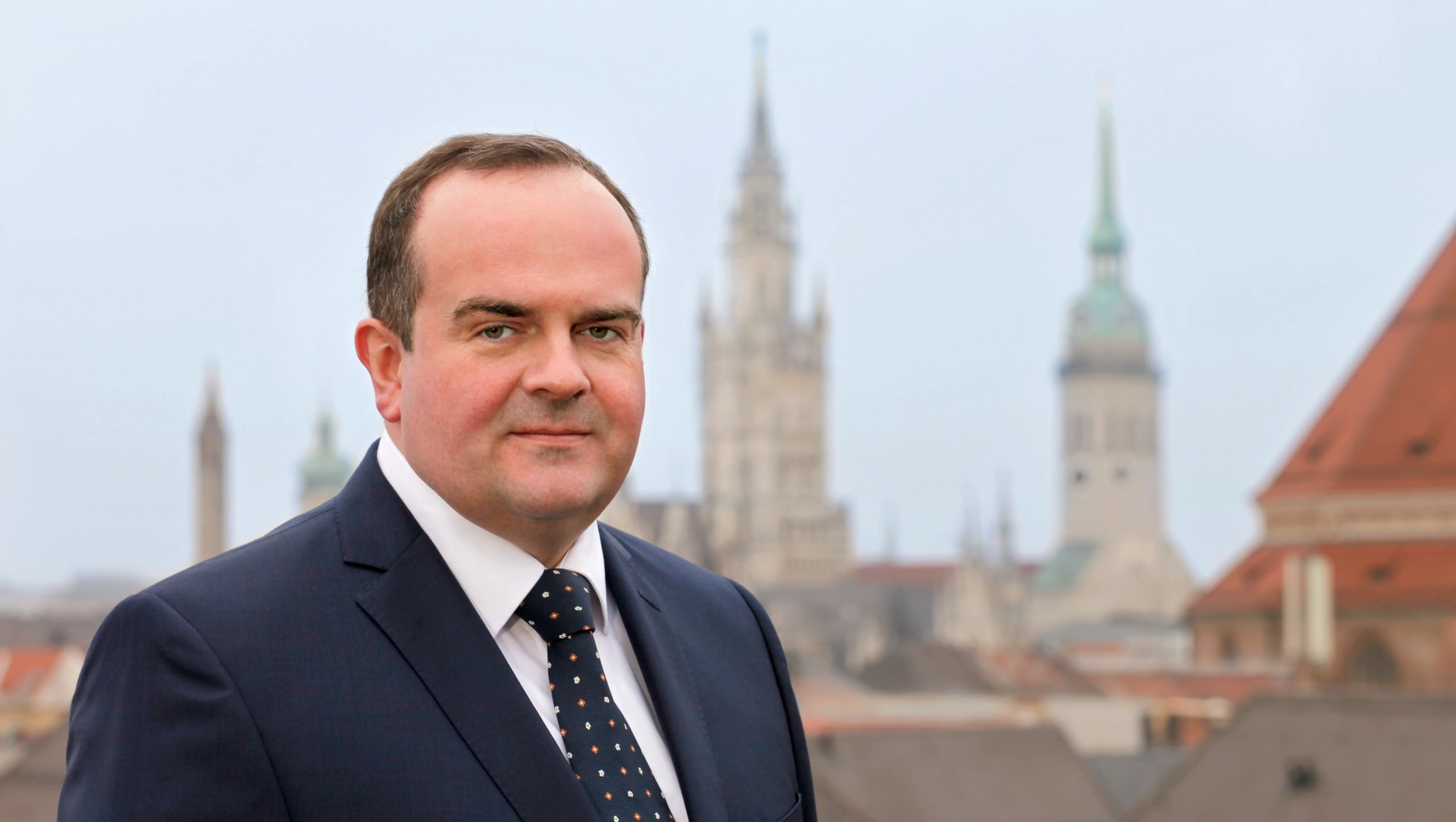 Foto mit Clemens Baumgärtner im Anzug vor den Dächern Münchens